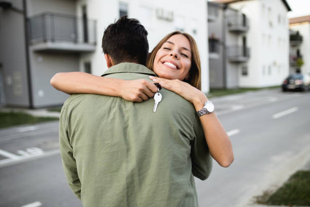 Happy young couple with key standing outside in front of their new home.